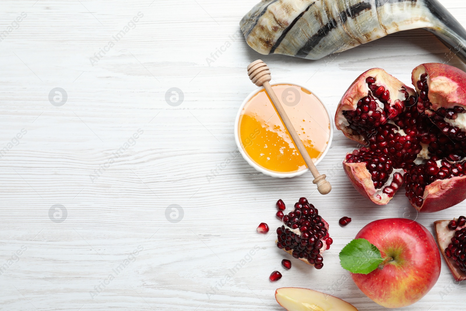 Photo of Honey, pomegranate, apples and shofar on white wooden table, flat lay with space for text. Rosh Hashana holiday