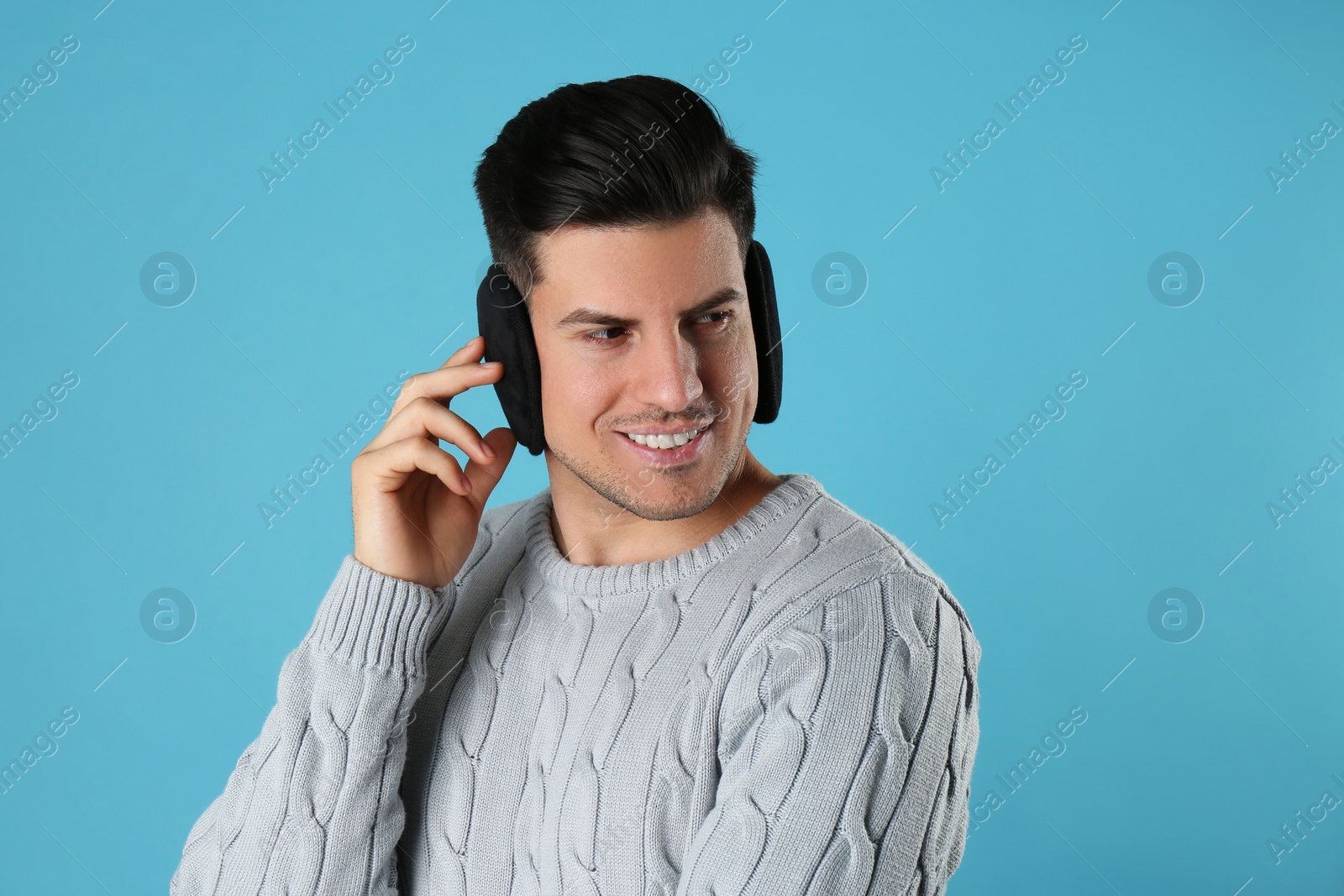 Photo of Man wearing stylish earmuffs on light blue background
