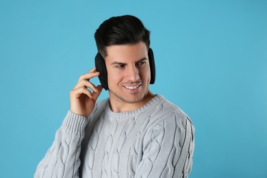 Man wearing stylish earmuffs on light blue background