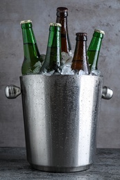 Photo of Metal bucket with bottles of beer and ice cubes on grey table