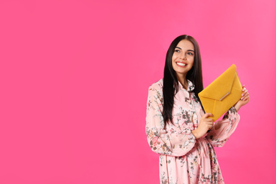 Photo of Young woman wearing floral print dress with elegant clutch on pink background. Space for text