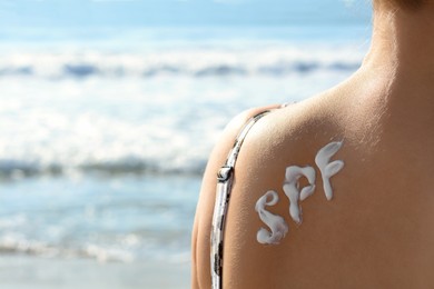 Woman with sun protection cream on her back at beach, closeup. Space for text