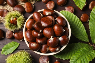 Photo of Fresh sweet edible chestnuts on brown wooden table, flat lay