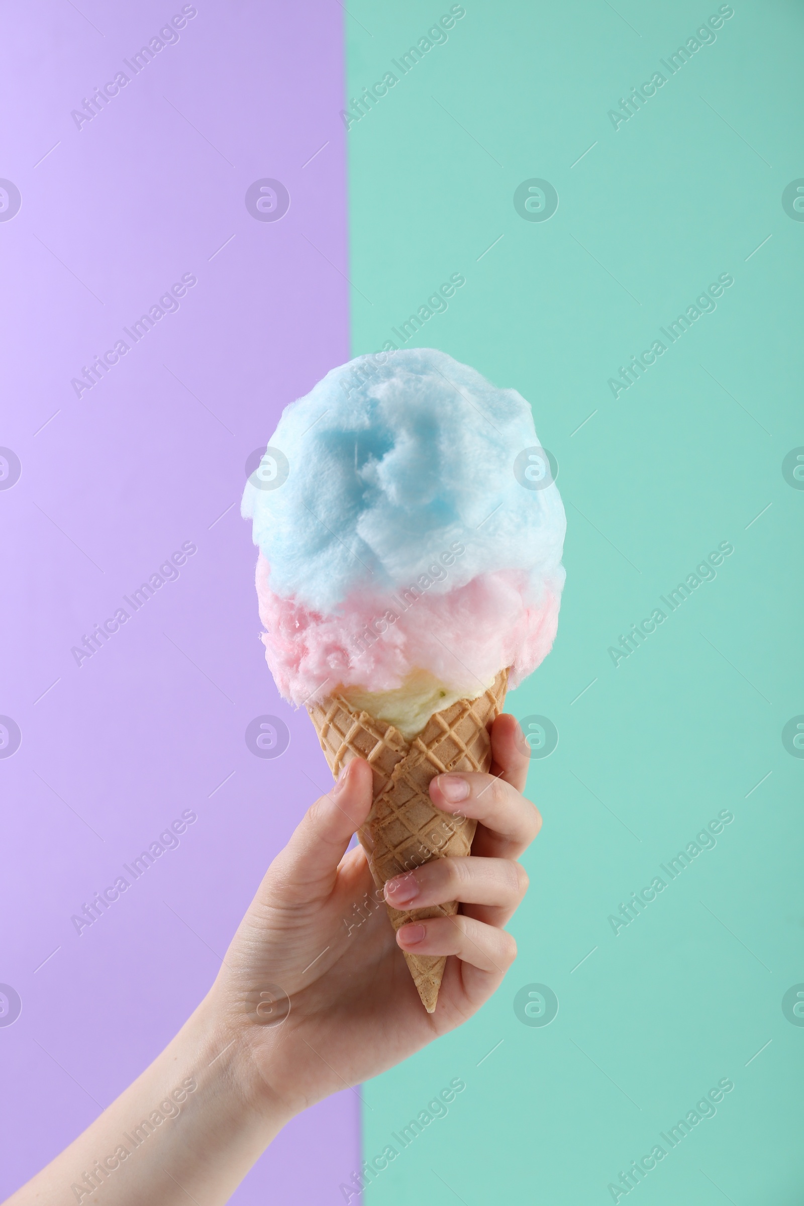 Photo of Woman holding waffle cone with cotton candy on color background, closeup