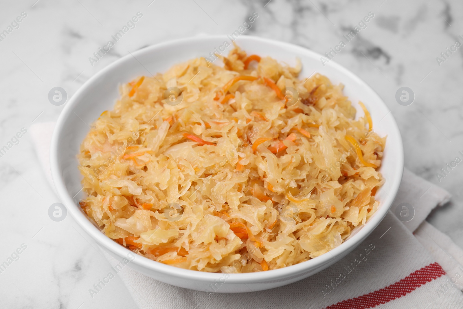 Photo of Bowl with tasty sauerkraut on white marble table, closeup