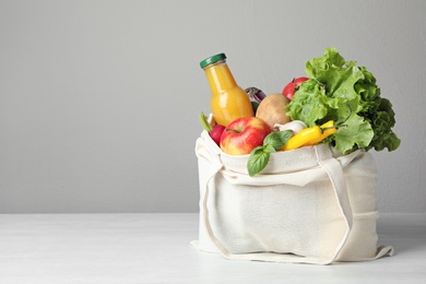 Photo of Cloth bag with vegetables and bottle of juice on table against grey background. Space for text