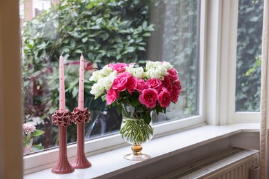 Vase with beautiful bouquet of roses and candles on windowsill indoors, space for text