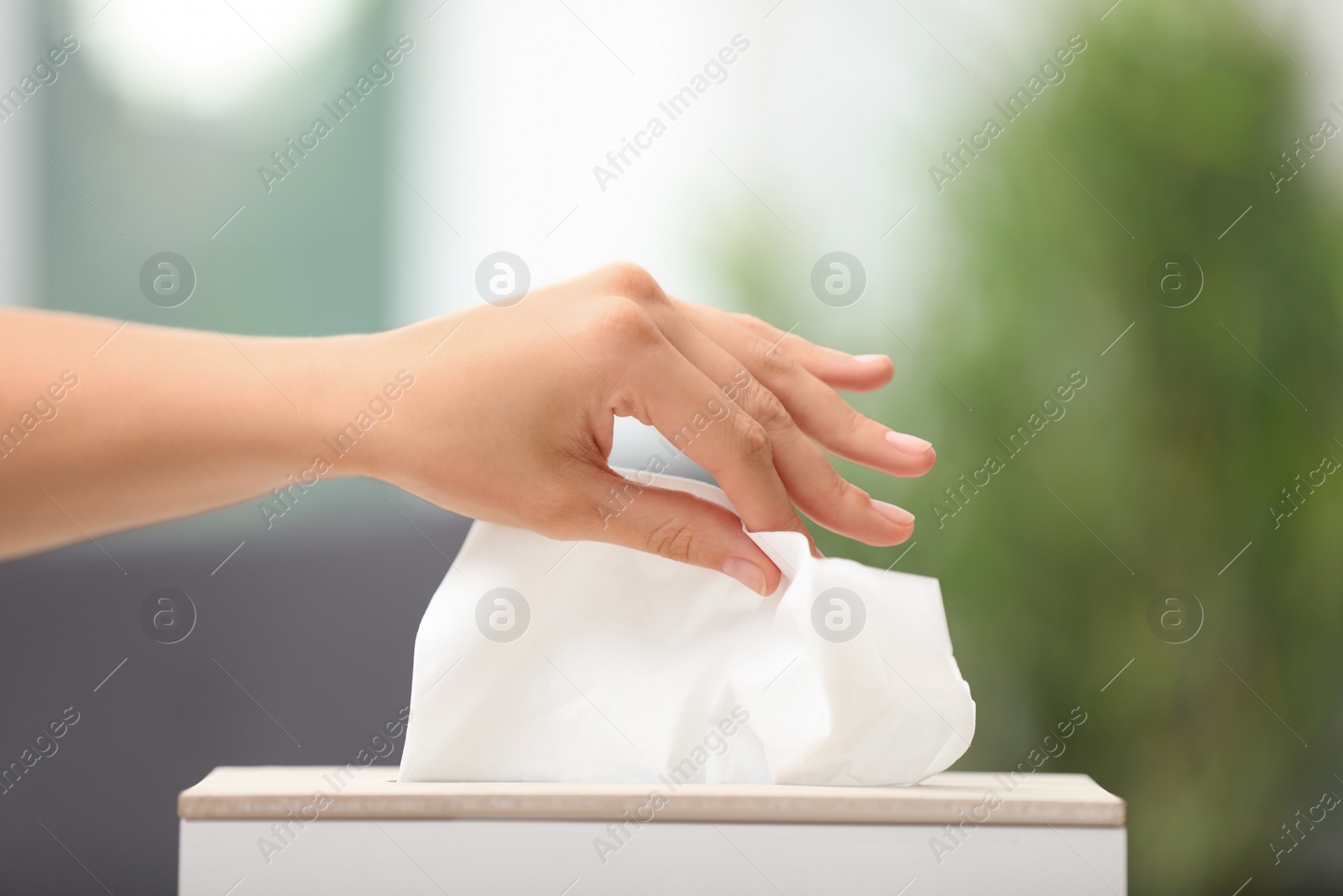 Photo of Woman taking paper tissue from holder on blurred background, closeup