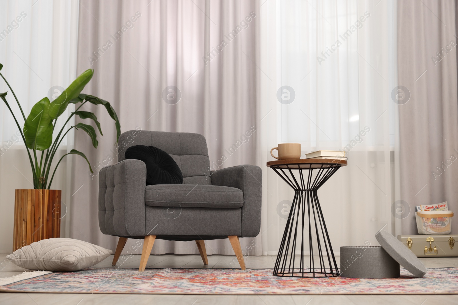 Photo of Stylish gray armchair and small table in living room. Interior design