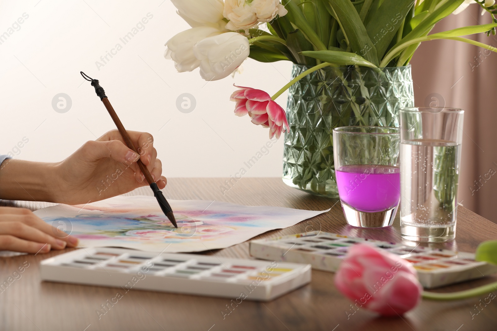 Photo of Woman painting flowers with watercolor at wooden table indoors, closeup. Creative artwork