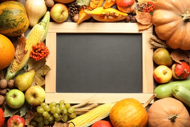 Chalkboard with space for text, autumn vegetables and fruits on wooden background, flat lay. Happy Thanksgiving day