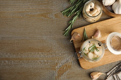 Photo of Flat lay composition with jars of pickled garlic on wooden table. Space for text