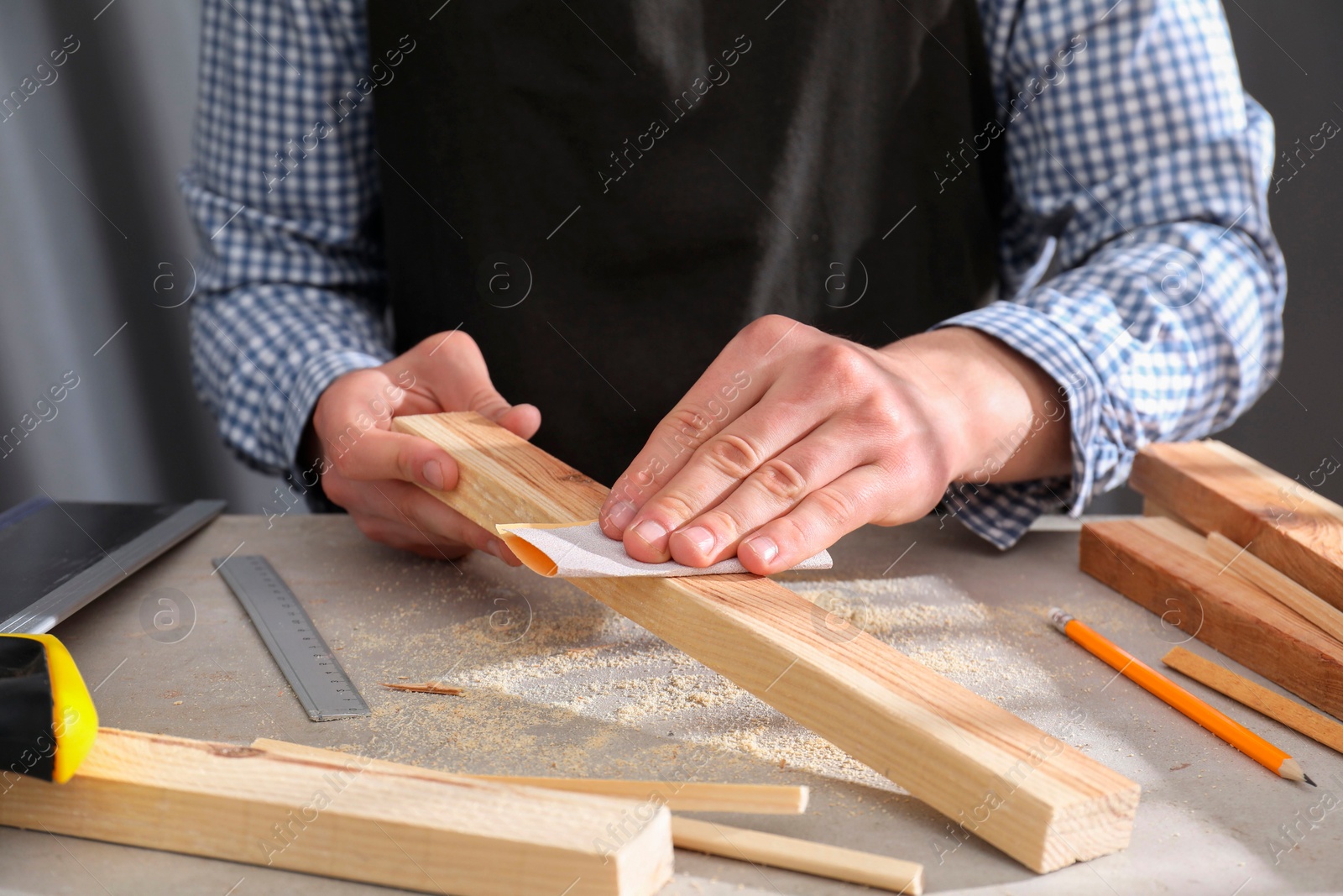 Photo of Man polishing wooden plank with sandpaper at grey table, closeup