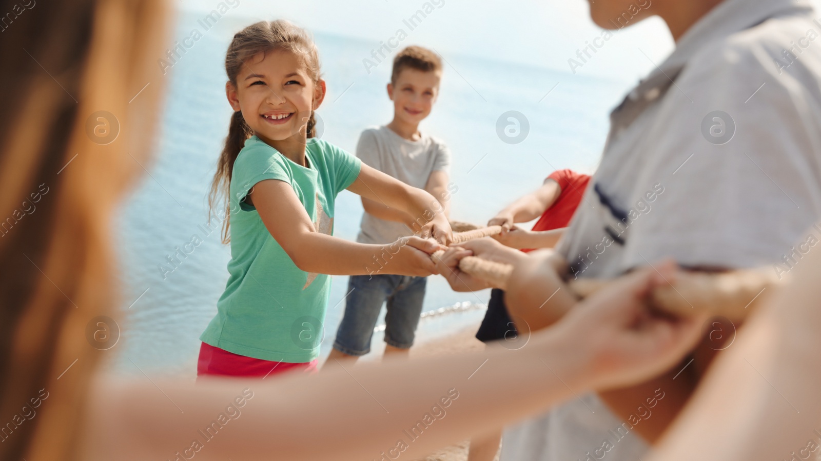 Image of Cute little children playing tug of war game near river on sunny day