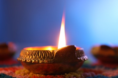 Photo of Diwali celebration. Diya lamp and colorful rangoli on table against blue background, closeup
