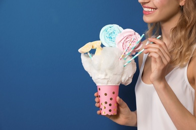 Young woman holding cotton candy dessert on blue background, closeup. Space for text