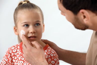 Photo of Father applying ointment onto his daughter's cheek on white background
