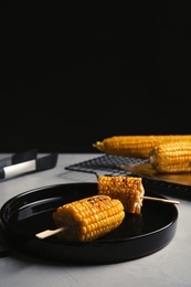 Photo of Ceramic plate with grilled corn cobs on light table against black background. Space for text