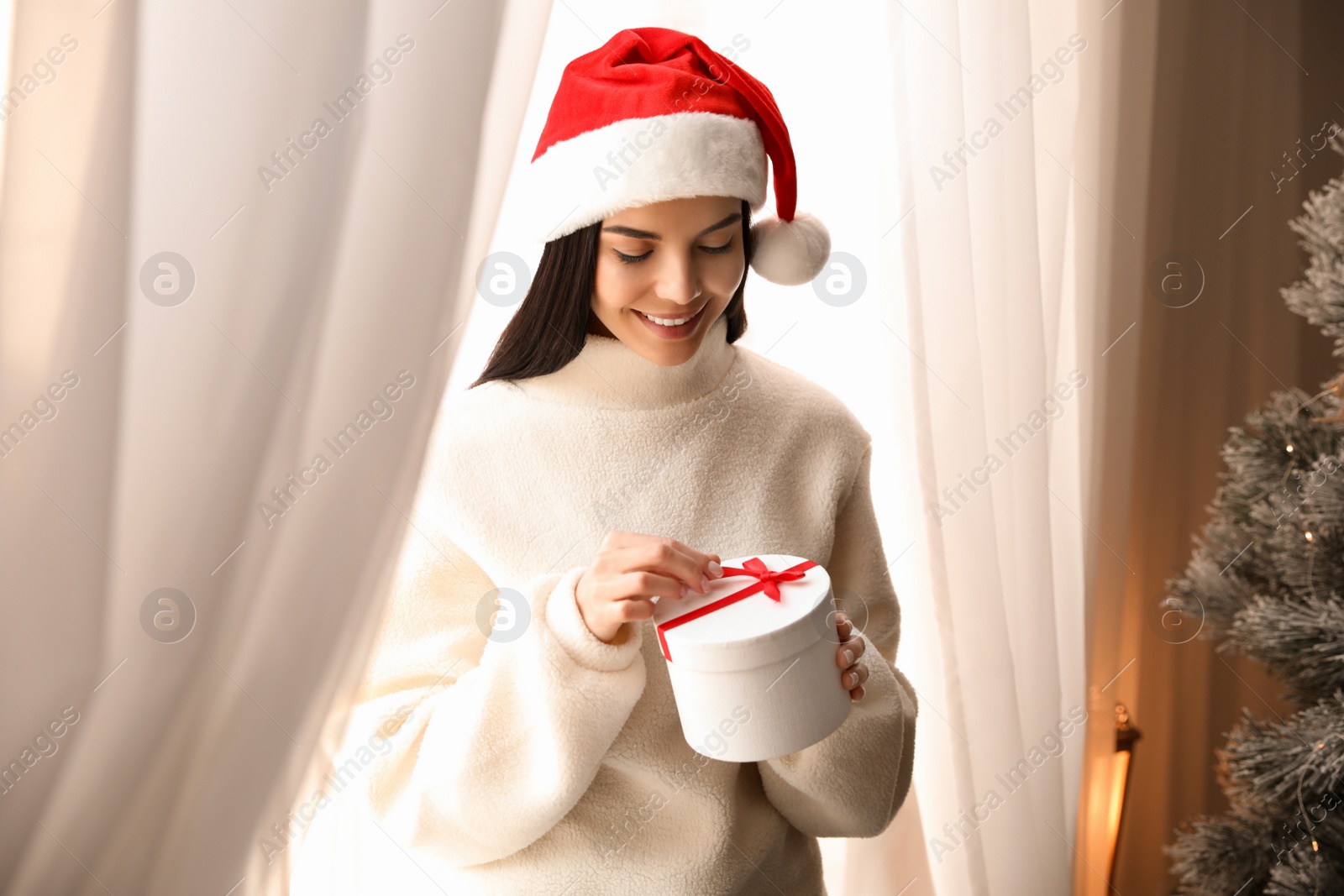 Photo of Woman in Santa hat opening gift box near Christmas tree