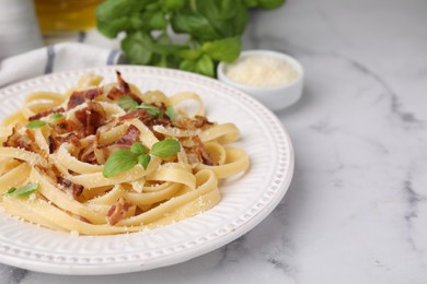 Tasty pasta with bacon and basil on white marble table, space for text