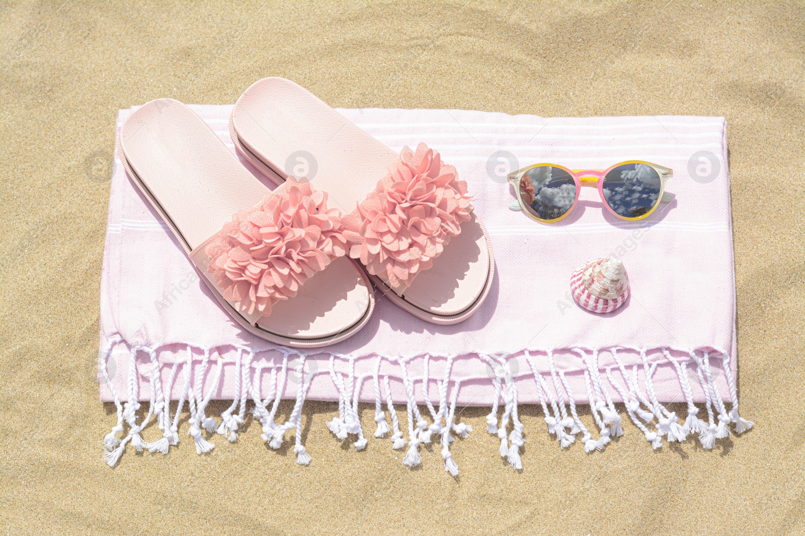 Photo of Blanket with slippers, sunglasses and seashell on sand outdoors, above view. Beach accessories