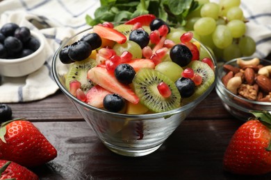 Photo of Tasty fruit salad in bowl and ingredients on wooden table, closeup