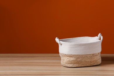 Empty wicker laundry basket near brown wall. Space for text
