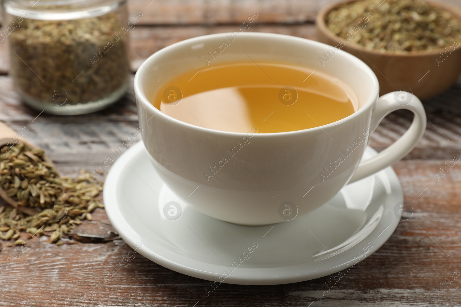 Photo of Aromatic fennel tea in cup and seeds on wooden table, closeup