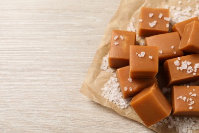 Photo of Tasty caramel candies and sea salt on light wooden table, above view. Space for text