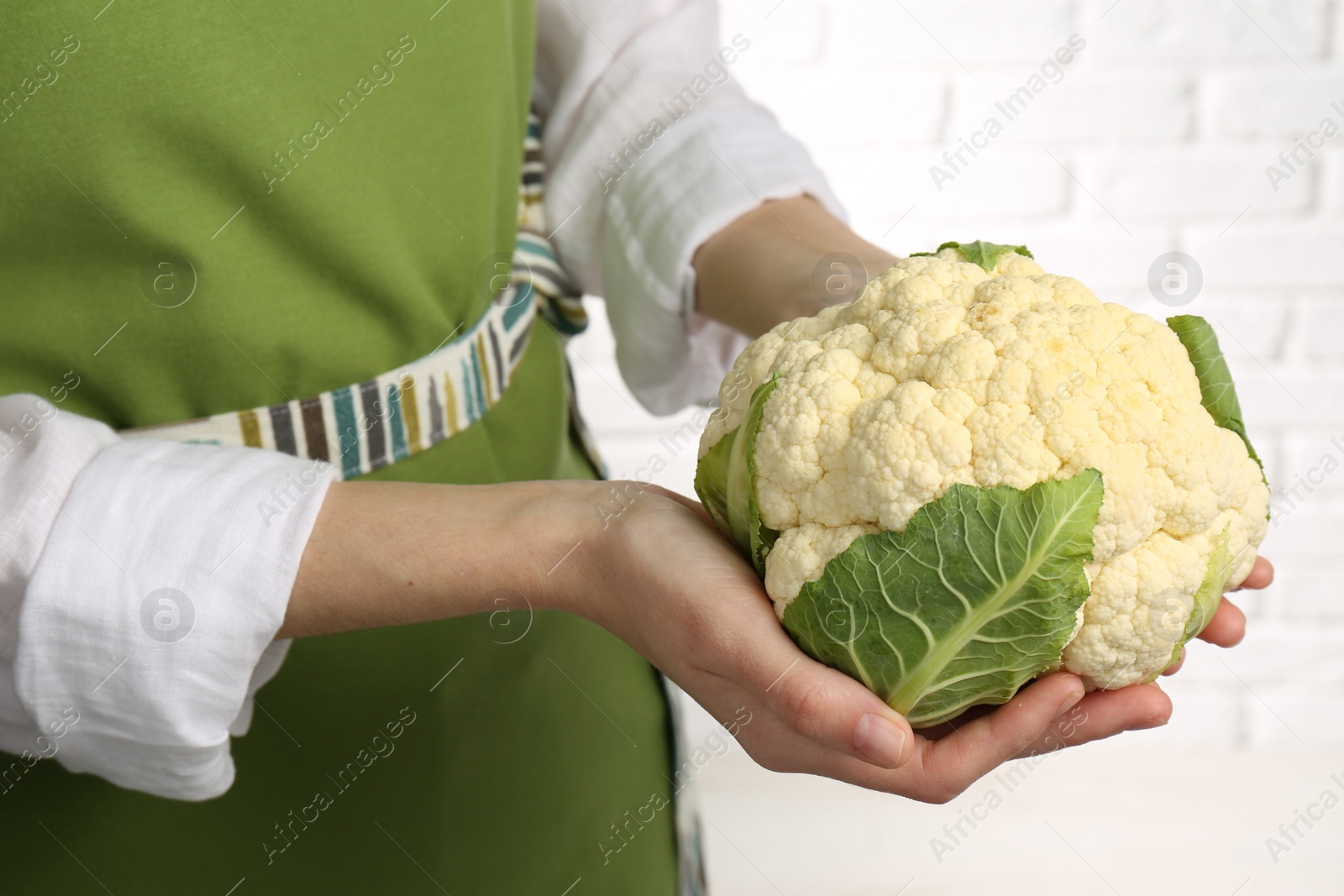 Photo of Woman holding fresh cauliflower against white brick wall, closeup