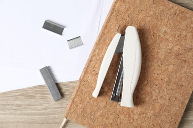 Stapler, paper, notebook and metal staples on wooden table, flat lay