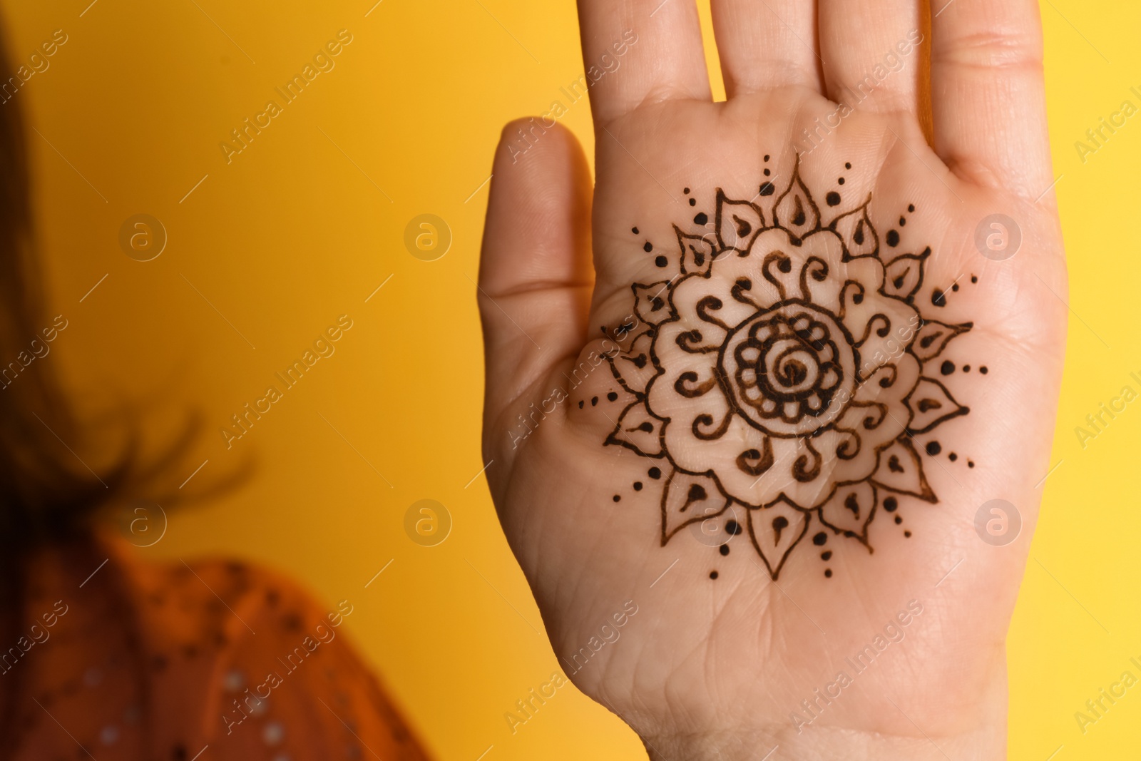 Photo of Woman with beautiful henna tattoo on hand against yellow background, closeup. Traditional mehndi