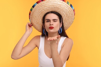 Photo of Young woman in Mexican sombrero hat blowing kiss on yellow background