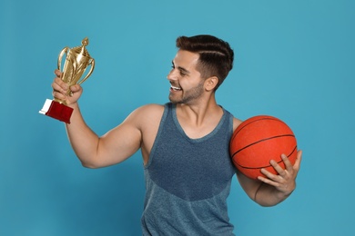 Photo of Portrait of happy young basketball player with gold trophy cup on blue background