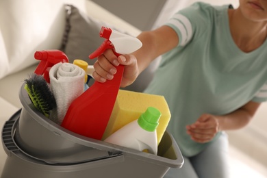 Photo of Woman taking bottle of detergent from bucket with cleaning supplies indoors, closeup