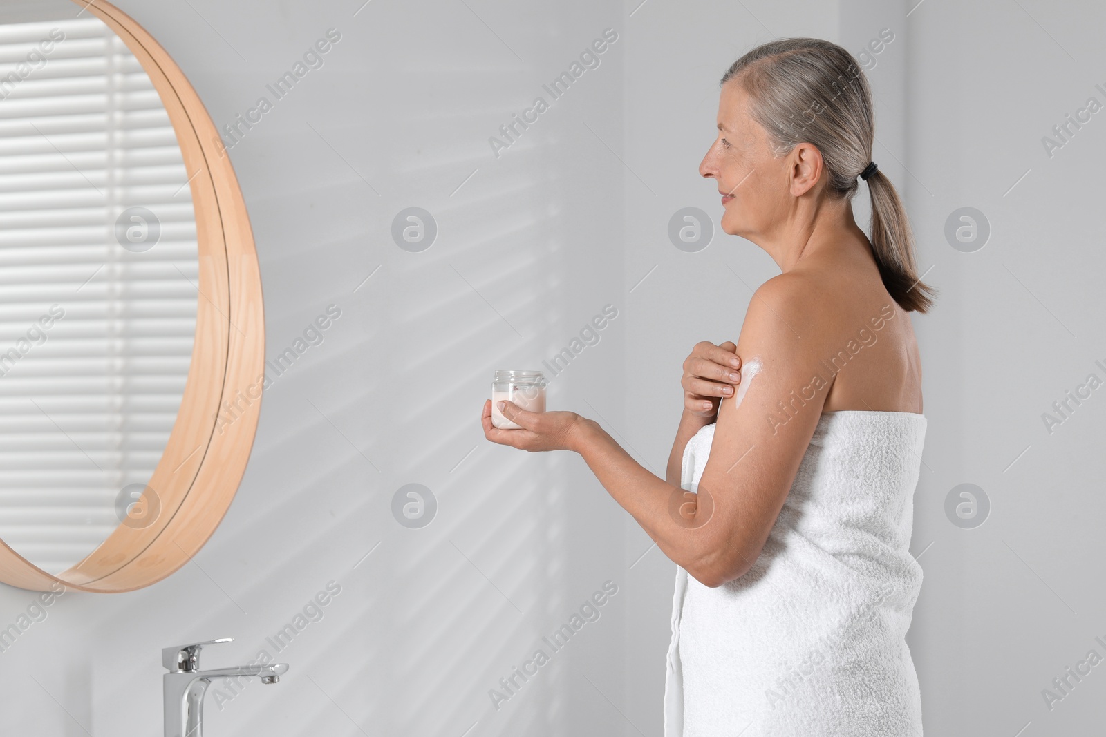 Photo of Happy woman applying body cream onto arm indoors. Space for text