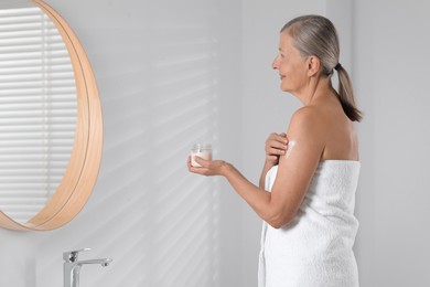 Photo of Happy woman applying body cream onto arm indoors. Space for text