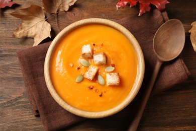 Photo of Bowl with tasty pumpkin cream soup on wooden table, flat lay