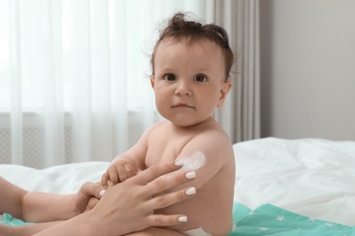 Photo of Mother applying body cream on her baby in bedroom
