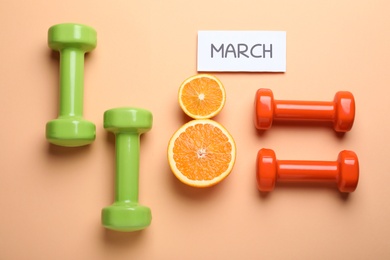 Photo of 8 March greeting card design with cut citrus and dumbbells on orange background, flat lay. International Women's day