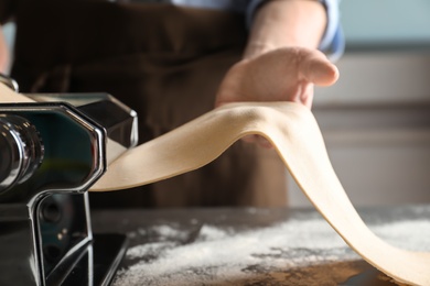 Young man preparing noodles on pasta maker at table