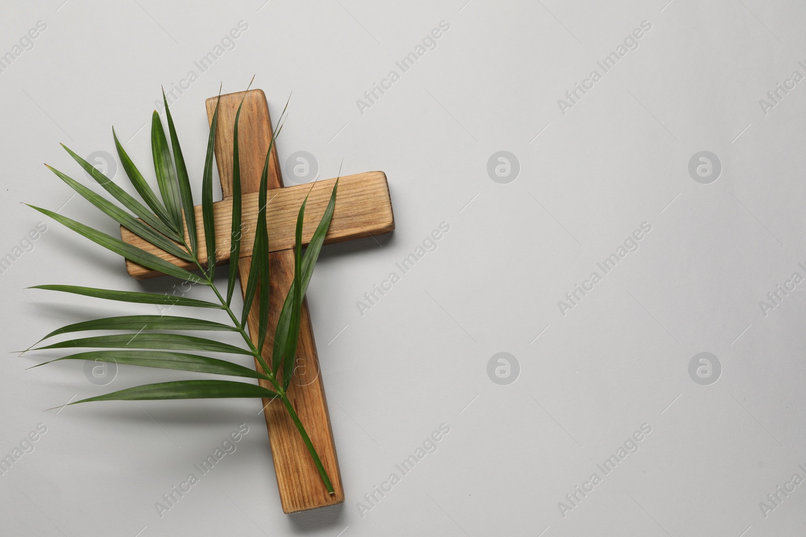 Photo of Wooden cross and palm leaf on light grey background, top view with space for text. Easter attributes