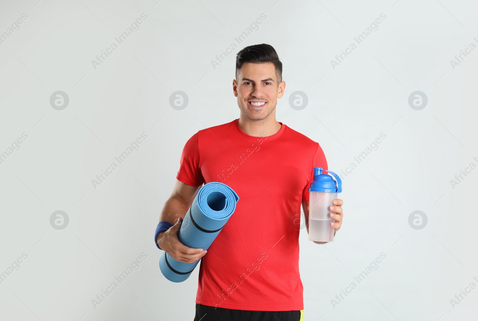 Photo of Handsome man with yoga mat and shaker on light background