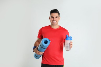 Photo of Handsome man with yoga mat and shaker on light background