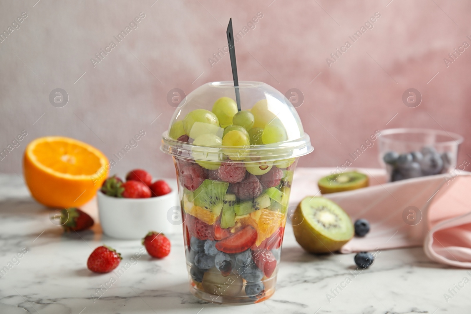 Photo of Fresh tasty fruit salad in plastic cup on white marble table