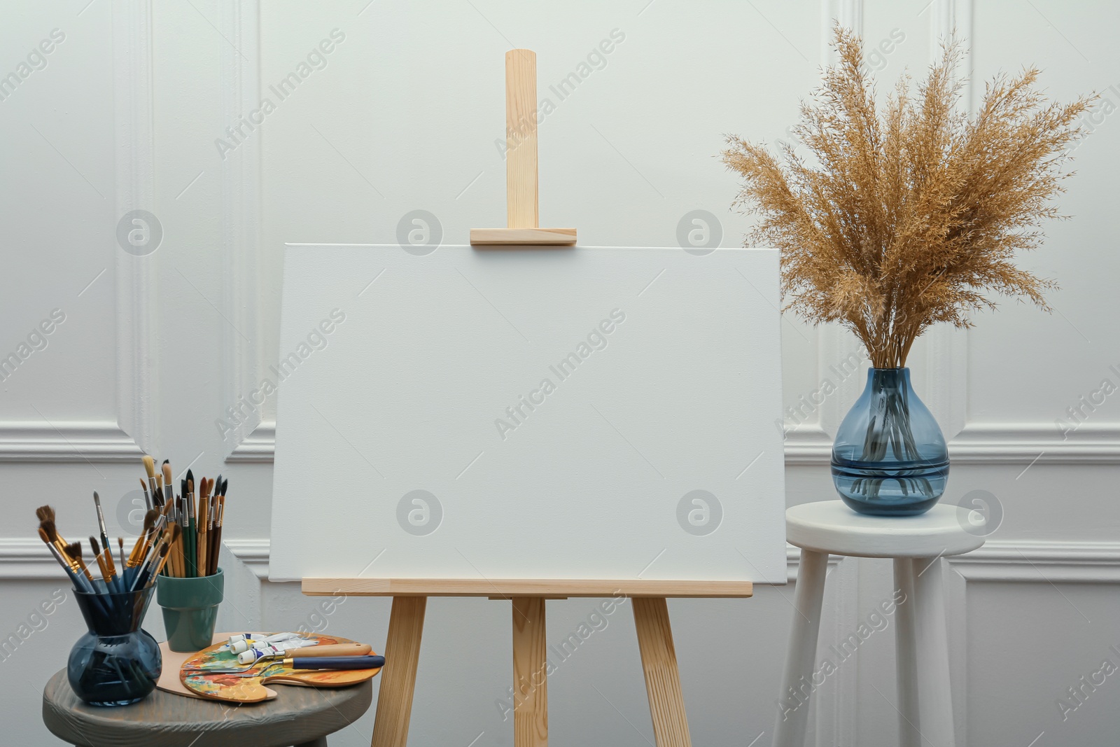 Photo of Easel with blank canvas, brushes, paints and palette in studio