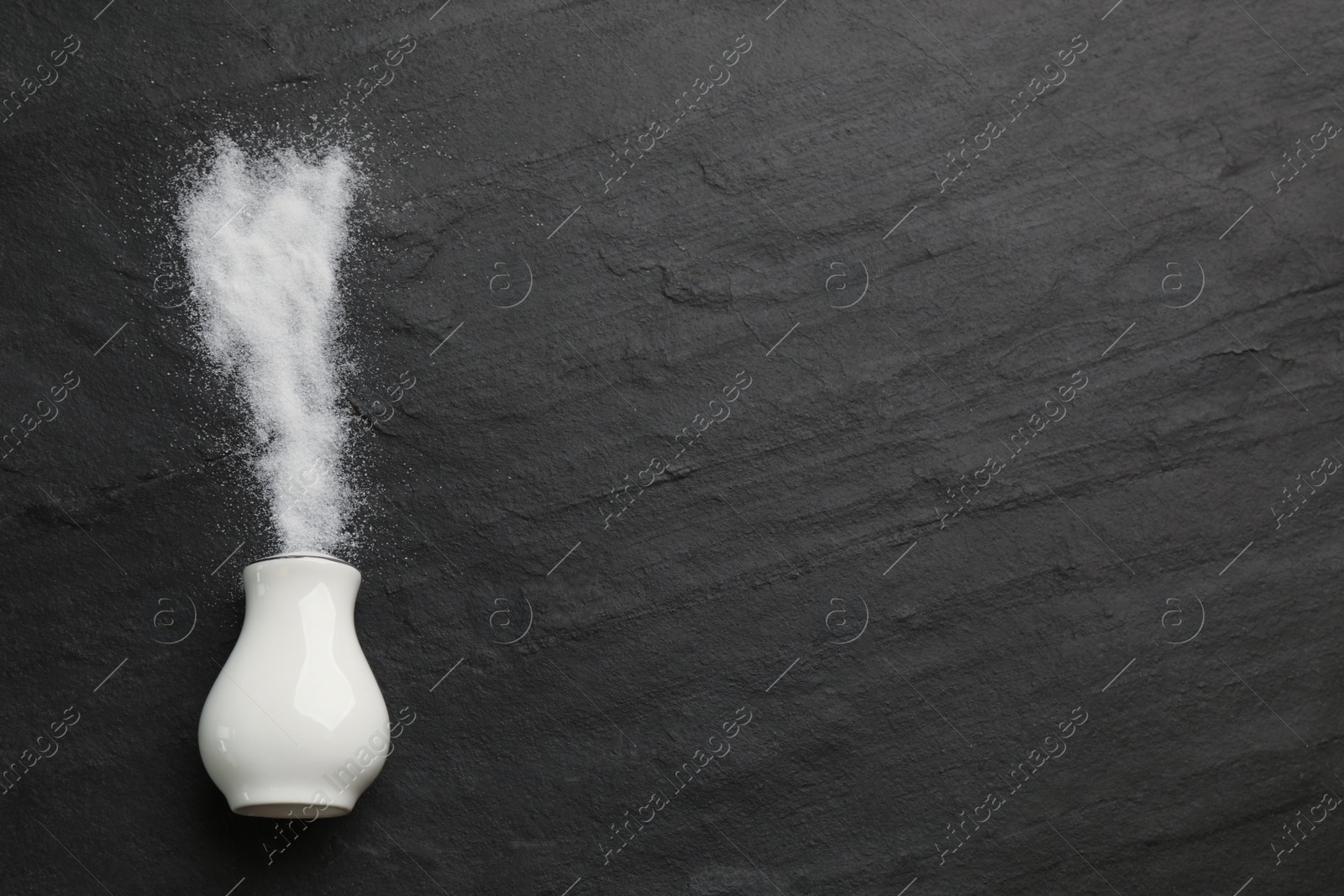 Photo of White ceramic salt shaker on black table, top view. Space for text
