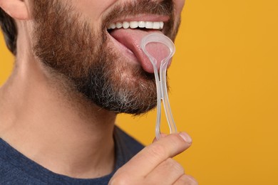 Man brushing his tongue with cleaner on yellow background, closeup. Space for text