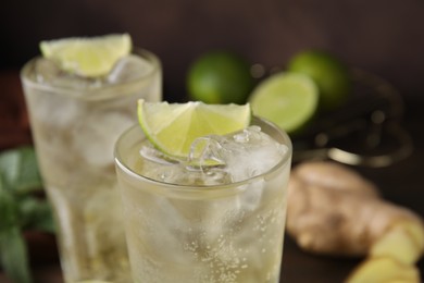 Glass of tasty ginger ale with ice cubes and lime slice on blurred background, closeup