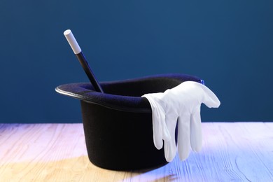 Photo of Magician's hat, wand and gloves on wooden table against blue background